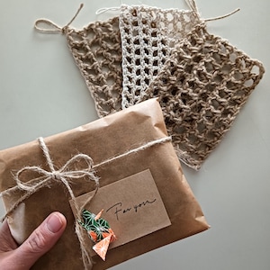 以下が含まれることがあります： 「For you」の文字が入った小さなタグと、カラフルな折り紙の鶴が付いた、茶色の紙で包まれた小包。2つの正方形の、オープンウィーブジュートコースターも表示されています。