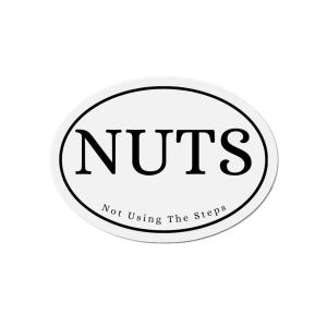 May include: Oval white sticker with a black border. The word "NUTS" is printed in bold, black letters. Below the word "NUTS" is the phrase "Not Using The Steps" in smaller, black text.