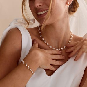 Puede incluir: Un delicado conjunto de joyería compuesto por un collar y una pulsera a juego, ambos con pequeñas perlas blancas intercaladas con diminutas cuentas doradas. También se observa un pequeño pendiente dorado con una perla blanca.