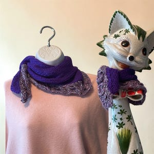May include: A knitted purple scarf with a textured border is displayed on a mannequin and a ceramic fox figurine. The scarf is a deep purple color with a lighter, speckled border. The fox figurine is white with green accents.
