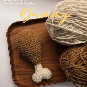 May include: A crocheted chicken leg in brown and white sits on a wooden tray, with cream and brown yarn balls. The word "Yummy" is written in yellow cursive. The text "MAOXIANCIKE" is printed at the bottom of the tray.