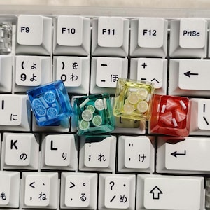 Peut inclure: Gros plan sur un clavier avec des touches personnalisées. Les touches sont transparentes et contiennent des motifs miniatures de roues, de tranches de citron vert, de tranches de citron et de fraises. Les touches sont bleues, vertes, jaunes et rouges.