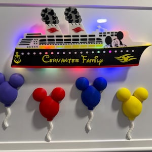 May include: A framed wall art piece featuring a lit-up cruise ship with the text "Cervantes Family" and a Mickey Mouse character graphic. Below the ship are four 3D-printed Mickey Mouse-shaped balloons in purple, red, blue, and yellow colours.