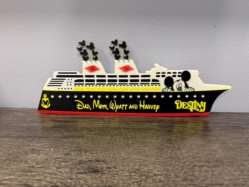 May include: A decorative cruise ship cutout featuring a black hull with a yellow anchor and the text "Dad, Mom, Wyatt and Harvey" and "Destiny" in yellow. The white upper deck includes two smokestacks with black Mickey Mouse head smoke clouds.