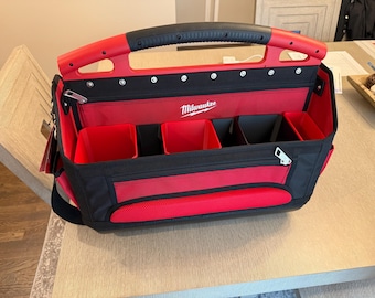 May include: Red and black Milwaukee tool bag with multiple compartments and a zipped pocket. The bag has a sturdy handle and the Milwaukee logo is visible on the front. The bag is designed for organising and carrying tools.