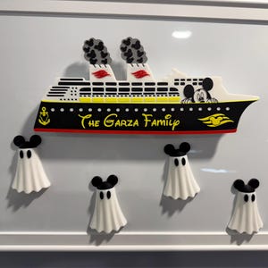 May include: A framed wall art piece featuring a cruise ship with black, white, yellow, and red details. The ship displays the text 'The Garza Family' and a Mickey Mouse silhouette. Below the ship are four white ghost figures with black Mickey Mouse ears.