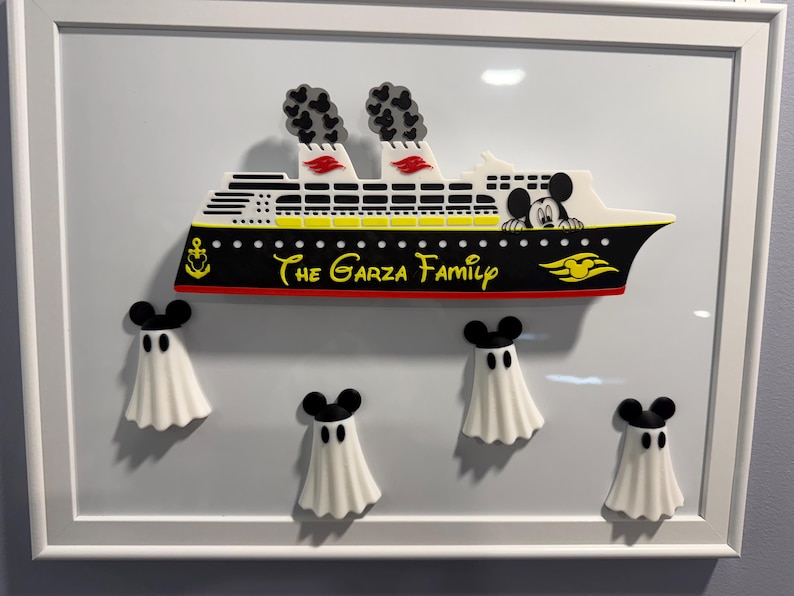 May include: A framed wall art piece featuring a cruise ship with black, white, yellow, and red details. The ship displays the text 'The Garza Family' and a Mickey Mouse silhouette. Below the ship are four white ghost figures with black Mickey Mouse ears.