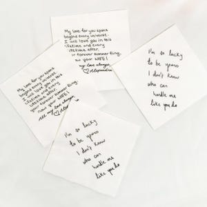 Könnte beinhalten: Vier weiße quadratische Servietten mit handgeschriebenen Nachrichten in schwarzer Tinte. Zwei Servietten tragen die Botschaft "My love for you spans beyond every universe..." und die anderen beiden sagen "I'm so lucky to be yours..."