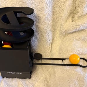 May include: A black ball track toy with a spiral track and a box base. The toy features a yellow ball and a red ball. The text "EastRack.co.uk" is printed on the base.