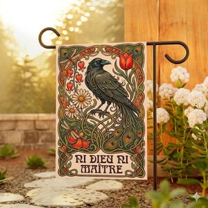 Può includere: Una bandiera da giardino decorativa con un'illustrazione dettagliata di un corvo appollaiato su un ramo, circondato da fiori e foglie. La bandiera presenta il testo "Ni Dieu Ni Maître" ed è esposta su un supporto in metallo nero.