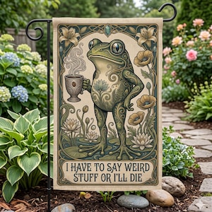 Op de afbeelding: Een tuinvaandel met een grillige illustratie van een kikker die een kop koffie vasthoudt. De kikker is versierd met ingewikkelde bloempatronen en de tekst luidt: "I HAVE TO SAY WEIRD STUFF OR I'LL DIE." De vlag wordt buiten getoond.