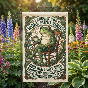 May include: A cream-coloured garden flag with a green frog in a wooden chair, holding a cup of coffee. The flag has text that reads "I caught the woke mind virus and all I got was empathy and critical thinking skills." The flag has a decorative border.
