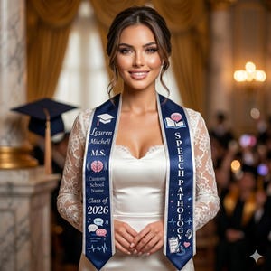 May include: A woman wearing a white dress and a navy blue graduation sash with the text "Speech Pathology." The sash also includes the name "Lauren Mitchell," the degree "M.S.," and "Class of 2026."