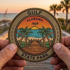 May include: Round embroidered patch featuring a beach scene with palm trees, a boardwalk, and the text "GULF ALABAMA 1939 STATE PARK." The patch has a tan border and a colorful sunset design.
