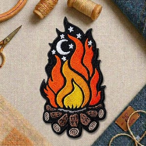 May include: Embroidered patch featuring a campfire design with flames in shades of orange, yellow, and red, topped with a crescent moon and stars. The patch includes a black border and brown logs at the base, perfect for adding to clothing or accessories.