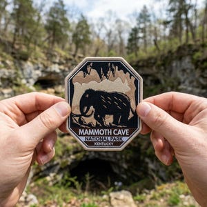 May include: An octagonal patch featuring a black woolly mammoth illustration. The patch has a tan border and a brown and tan background depicting a cave. Text at the bottom reads "MAMMOTH CAVE NATIONAL PARK KENTUCKY."