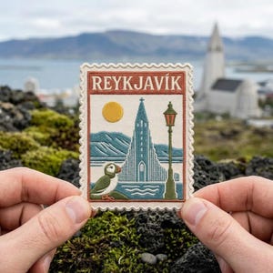May include: A rectangular embroidered patch with a scalloped edge featuring the text REYKJAVÍK. The design depicts a tall church, a yellow sun, a green puffin, and a lamp post in shades of blue, green, and cream against a white background.