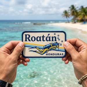 May include: A rectangular patch with the word "Roatán" in blue and a diver illustration. The patch has a blue border and the word "HONDURAS" at the bottom. The background shows a beach and ocean.