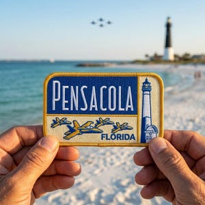 May include: A rectangular patch with the word "PENSACOLA" in white letters on a blue background. Below are yellow and blue airplane designs and the word "FLORIDA". A lighthouse illustration is on the right. The patch is held up against a beach background.
