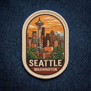 May include: An oval embroidered patch featuring a detailed Seattle skyline with the Space Needle, city buildings, and a mountain peak under an orange sky. The text SEATTLE WASHINGTON is stitched in white at the bottom against a dark red background.