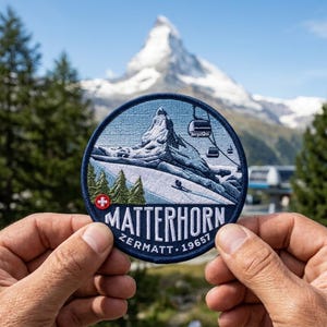May include: A circular embroidered patch featuring a detailed depiction of the Matterhorn mountain, a ski lift, and green pine trees. The text "MATTERHORN ZERMATT 19657" is stitched in white at the bottom, accompanied by a small red Swiss flag emblem.