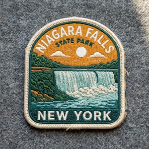 May include: An embroidered patch featuring a landscape of Niagara Falls State Park. The design includes a golden sky with a white sun, green trees, a cascading waterfall, and the text NIAGARA FALLS STATE PARK and NEW YORK in white thread.