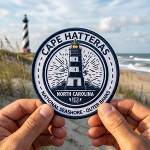 May include: Round patch with a lighthouse design. The patch features the text "Cape Hatteras National Seashore - Outer Banks, North Carolina" and "ESTD 1953". The lighthouse is black and white with a yellow light.