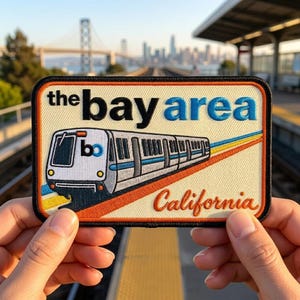 May include: Embroidered patch featuring a train and the words "the bay area California". The patch has a cream background with a black border. The train is white and blue, with orange, yellow, and blue stripes.