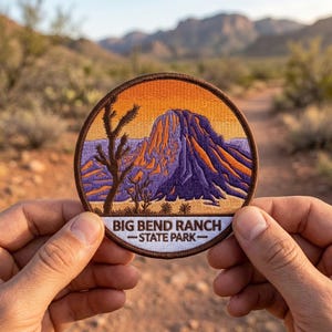 May include: A circular embroidered patch featuring a desert landscape with a large purple mountain, a dark brown silhouette of a desert tree, and an orange sky. The white bottom section contains the text BIG BEND RANCH STATE PARK in black.