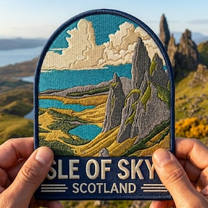May include: Embroidered patch featuring a scenic landscape of the Isle of Skye, Scotland. The patch has a blue border and depicts mountains, water, and clouds in shades of gray, green, yellow, and blue. The text "ISLE OF SKY SCOTLAND" is at the bottom.