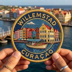 May include: A circular embroidered patch featuring a colorful cityscape of Willemstad, Curaçao, with yellow, red, and blue buildings along a waterfront. A small boat filled with produce floats in the foreground. The text WILLEMSTAD CURAÇAO is stitched in gold.