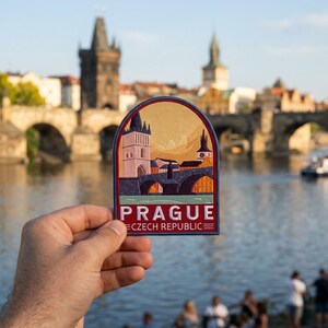 May include: Embroidered patch featuring a Prague cityscape with a bridge, buildings, and the text "PRAGUE CZECH REPUBLIC". The patch has a red, blue, and gold color scheme, with a dark blue border.