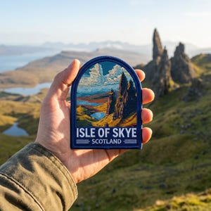May include: A blue patch with the text "Isle of Skye Scotland" and an image of the Scottish landscape. The patch features a mountain range, a lake, and a blue sky with clouds. The patch is held in a hand.