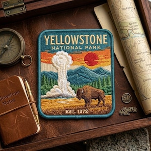 May include: A square embroidered patch featuring the text YELLOWSTONE NATIONAL PARK and EST. 1872. The design depicts a geyser erupting, a brown bison, green pine trees, blue mountains, and a red sun against an orange and yellow sky.