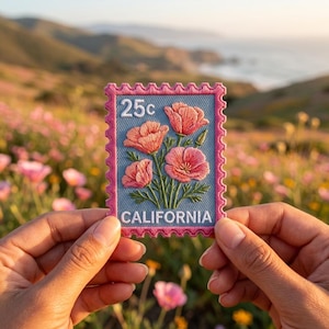 May include: A rectangular embroidered patch shaped like a postage stamp with a scalloped pink border. The center features a light blue background with pink California poppy flowers, green stems, the text 25c, and the word CALIFORNIA in white.