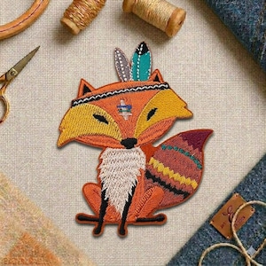 May include: Embroidered patch of a fox wearing a Native American headdress. The fox is orange, yellow, and white with a black nose and eyes. The patch has a detailed design with colorful feathers and a patterned tail.