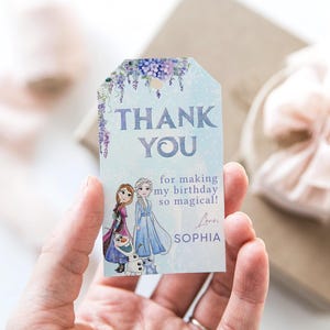 Könnte beinhalten: Ein hellblaues Etikett mit den Worten "THANK YOU" in großen, lila Buchstaben. Das Etikett zeigt Illustrationen von zwei Zeichentrickfiguren und den Text "for making my birthday so magical!" und den Namen "SOPHIA".