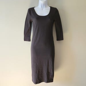 May include: A dark gray, knee-length dress with a scoop neckline and three-quarter sleeves. The dress is displayed on a white mannequin against a neutral background. The dress appears to be made of a soft, stretchy material.