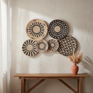 Puede incluir: Un conjunto de seis cestas de pared redondas tejidas con patrones geométricos en color beige natural y negro, dispuestas en grupo. Las cestas muestran varios diseños, incluyendo rayos de sol, círculos concéntricos y líneas en zigzag con textura.