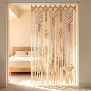 Könnte beinhalten: Ein großer Makramee-Wandbehang oder Raumteiler aus cremefarbenem Baumwollgarn. Das Stück zeigt komplexe geometrische Knotenmuster, darunter Chevron-Designs, gedrehte vertikale Säulen und Rautenformen, die mit langen Fransenquasten abgeschlossen sind.