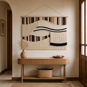 Peut inclure: Une grande tenture murale en macramé rectangulaire présentant un motif géométrique de cordes verticales et de sections tissées dans des tons crème, beige, marron et noir. L'œuvre est suspendue à une tige en bois avec une fine ficelle.