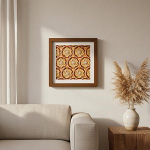 Può includere: Una stampa incorniciata con un motivo geometrico ripetuto in tonalità oro, rosso e marrone. L'opera d'arte è racchiusa in una cornice di legno marrone e appesa a una parete neutra. La stanza comprende anche un divano beige e un tavolino in legno.