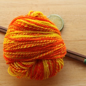 May include: A ball of orange and yellow yarn with wooden knitting needles and a lime slice.