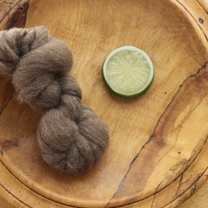 May include: A brown ball of wool yarn sits on a wooden plate with a slice of lime next to it.