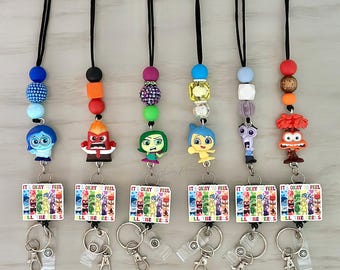 May include: A collection of lanyards featuring character charms and beaded accents. Each lanyard has a different character charm, including Anger, Sadness, Joy, and Fear. The lanyards also have a rectangular tag that reads "IT'S OKAY TO FEEL".