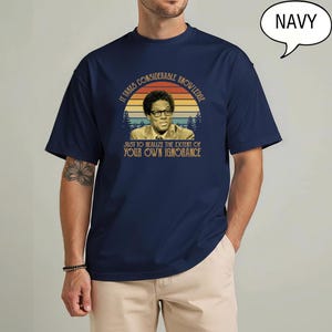 May include: Navy blue t-shirt featuring a vintage-style graphic of a man in glasses with the text "It takes considerable knowledge just to realize the extent of your own ignorance." The graphic is set against a sunset backdrop.