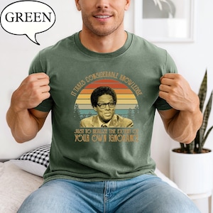 May include: Green t-shirt featuring a portrait of a man wearing glasses, set against a sunset design. The shirt includes the quote, "It takes considerable knowledge just to realize the extent of your own ignorance."