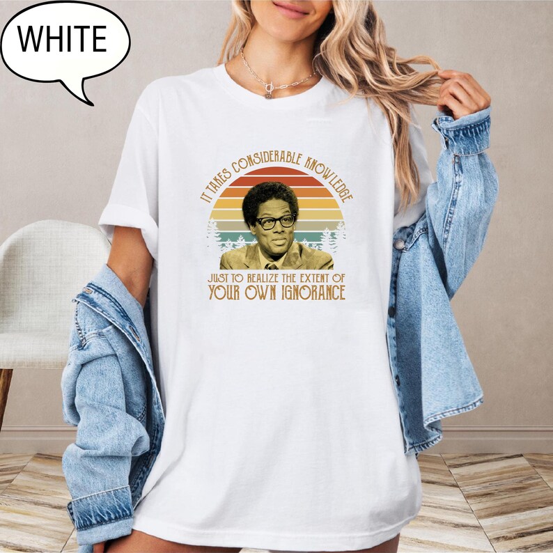May include: White t-shirt featuring a vintage-style graphic of a man in glasses with the text "IT TAKES CONSIDERABLE KNOWLEDGE JUST TO REALIZE THE EXTENT OF YOUR OWN IGNORANCE." The graphic is set against a sunset backdrop.
