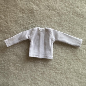 Puede incluir: Una peque&ntilde;a camisa blanca de manga larga con cuello redondo. La camisa est&aacute; hecha de una tela texturizada y tiene un dise&ntilde;o simple y cl&aacute;sico. Las mangas son largas y terminan con un dobladillo simple.
