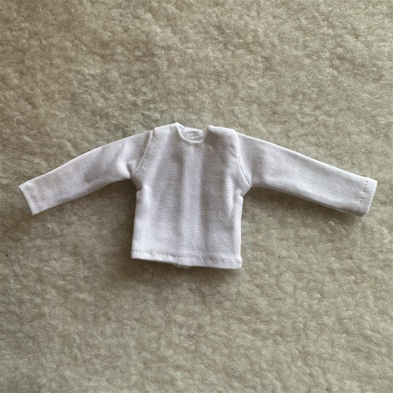 Puede incluir: Una peque&ntilde;a camisa blanca de manga larga con cuello redondo. La camisa est&aacute; hecha de una tela texturizada y tiene un dise&ntilde;o simple y cl&aacute;sico. Las mangas son largas y terminan con un dobladillo simple.